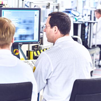 Two men in an electronics production area looking at a screen.