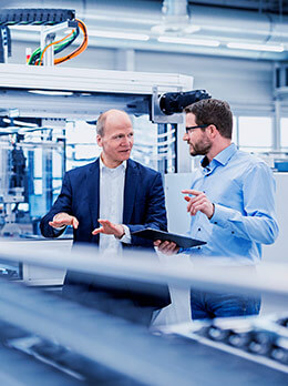 Two people analyzing industrial machine with tablet in automated production environment