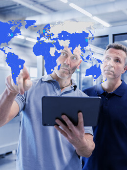 Two people analyzing global service processes on tablet with world map overlay in industrial environment